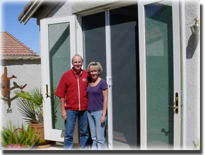 older couple standing in front f white french screen doors of home