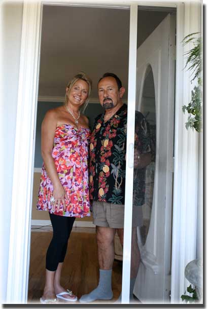Couple in bright colored patterned shirts standing in doorway of home opening a screen door