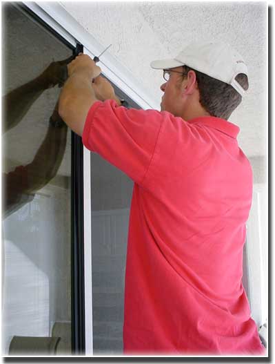 man with a red polo shirt and white cap working on top of a exterior screen door