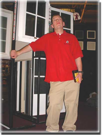 man with red polo and tan pants looking up various window frames behind him