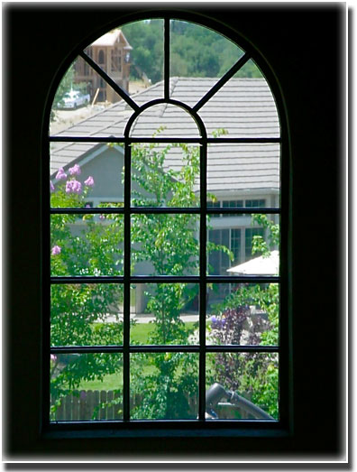 View through a arched window outside of home trees and other home are in view