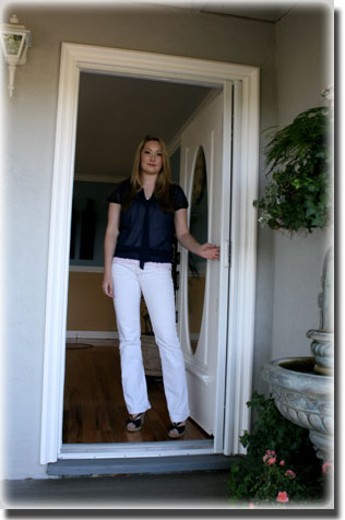 Woman standing in doorway of home wearing black shirt and white pants
