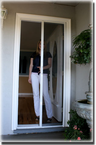 Woman has screen door pulled halfway across doorway of home