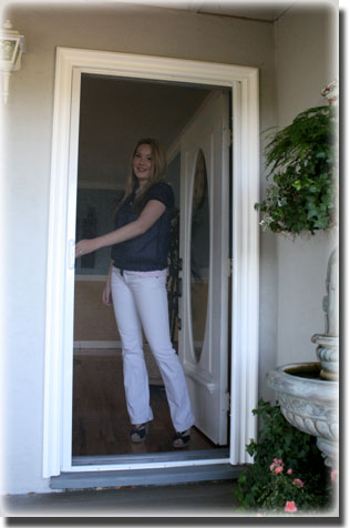 Woman standing behind fully closed screen front door of home