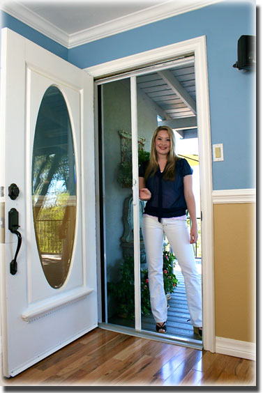 woman dressed in black and white with blonde hair standing in doorway of screen door into home