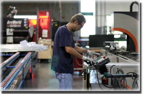 Man in t shirt and jeans working on tool in manufacturing line