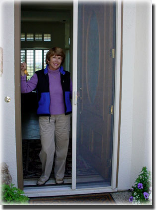 Older woman wearing blue and black sweater standing in door way of home showing off screen door