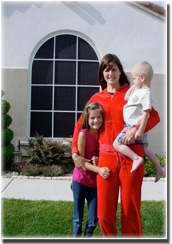 woman in red jumpsuit holding a toddler and hugging her daughter in front of windows