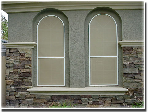 Custom Beige Privacy Screens on arch shaped widows of home bricks surround them