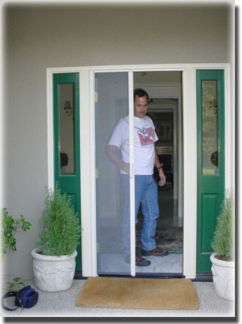 Man standing in doorway closing screen door plants in pots on porch