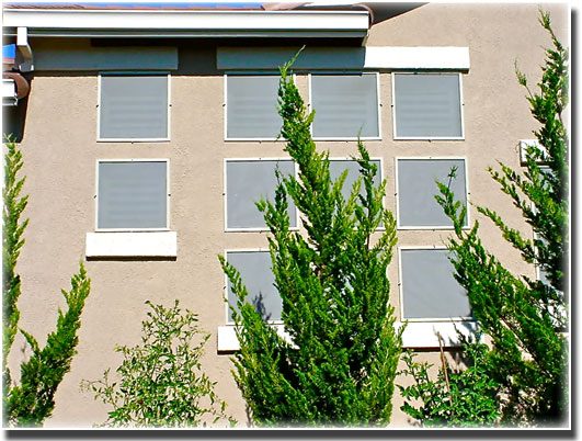 Grey Sun Screens installed in three rows of three square windows of home trees on the ground in front