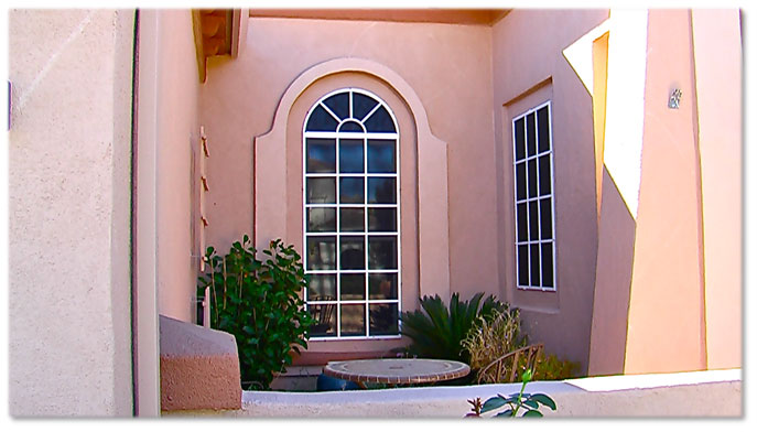 pink spanish style home with large windows that have sun screens