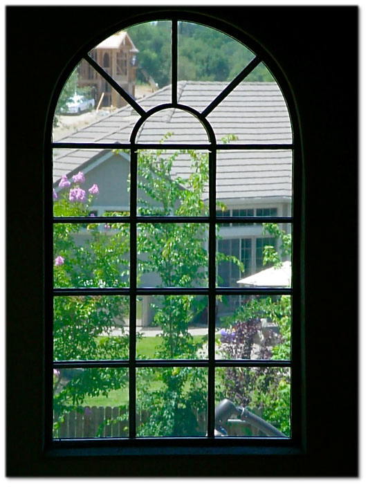 view out of window of home with arched sun screen we see trees and the home next door