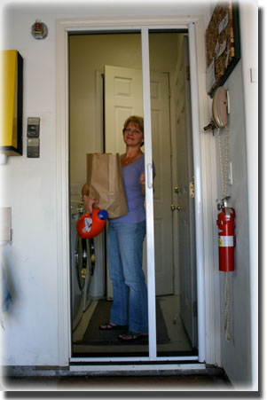 Woman holding brown paper bag standing behind screen door on front of home