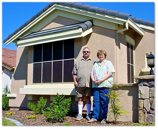 Older couple standing next to their home with black solar screens in windows