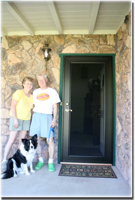older couple with their dog standing on front porch by security door