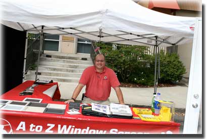 Man standing at booth with written materials and he is wearing a red shirt with glasses