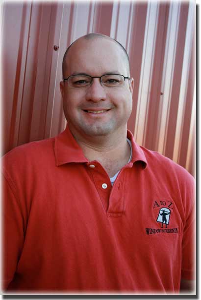 man in red polo shirt with glasses smiling and standing in front of a metal wall