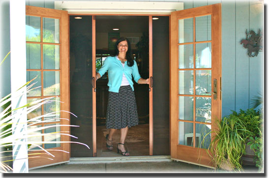 Woman in teal sweater and black skirt standing in doorway of out swing french doors