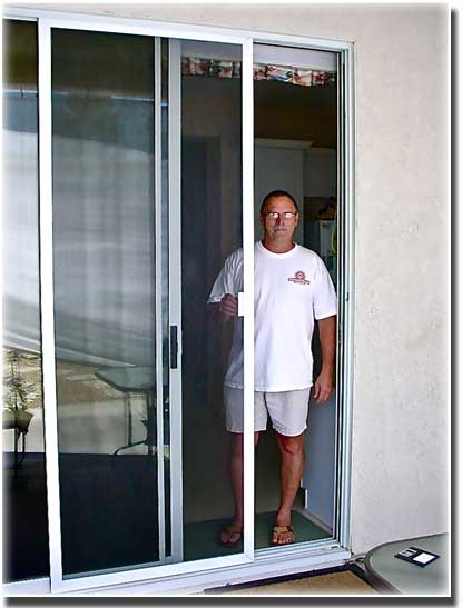 man in t shirt and shorts standing in a doorway of sliding screen door