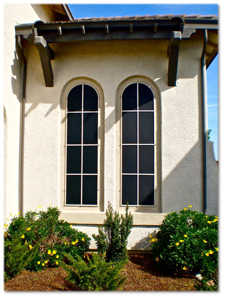 Two windows with sun screens spanish style home with bushes in front of windows