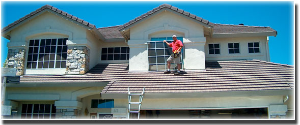 Home with man wearing red shirt standing on roof installing sun screens
