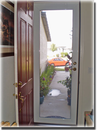 View from inside home out open front door the door is red and we see through the glass door and a red car on street