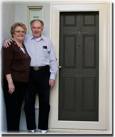 Elderly Couple Standing next to brown front door-