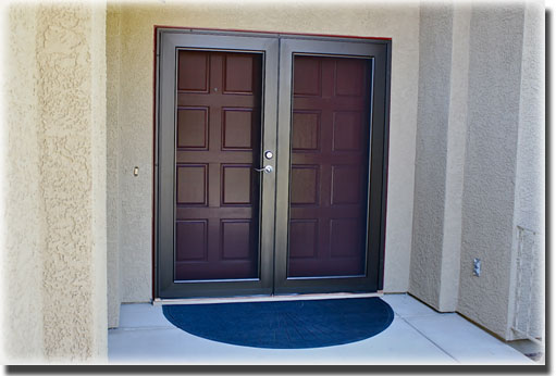Brown double french doors on front porch of home with black doormat
