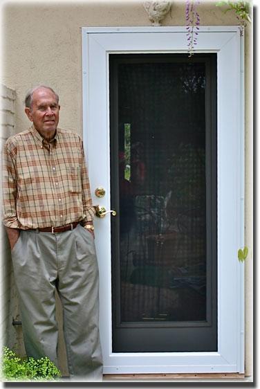 elderly man standing in front of black security door with white glass screen door