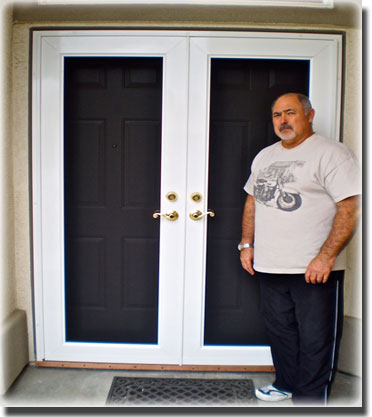 Man in tshirt and black pants standing in front of glass double doors with white trim