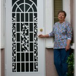 Older woman standing in front of decoritive white screen door