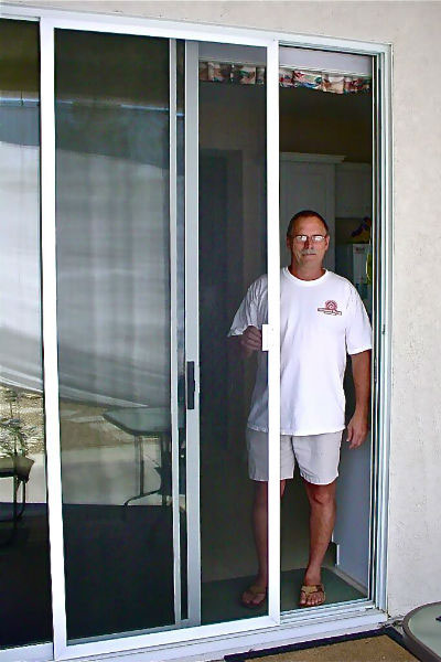 Man in shorts and white shirt standing in a sliding patio screen door