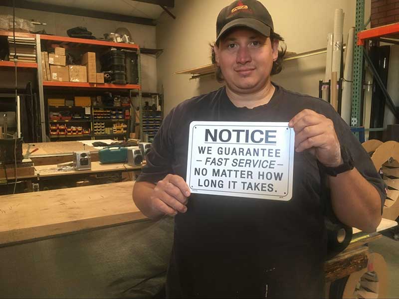 Man in black t shirt and hat holding up sign in workshop