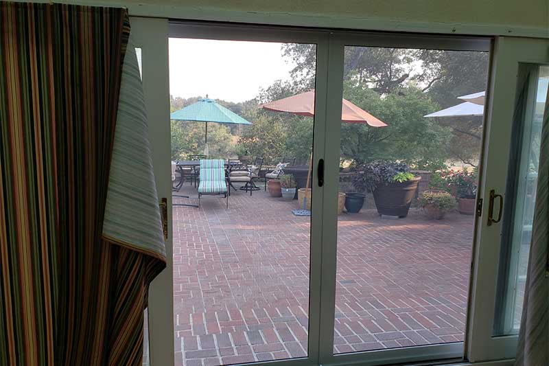 view out of two sliding screen doors we see beach umbrellas and chairs on brick concrete patio
