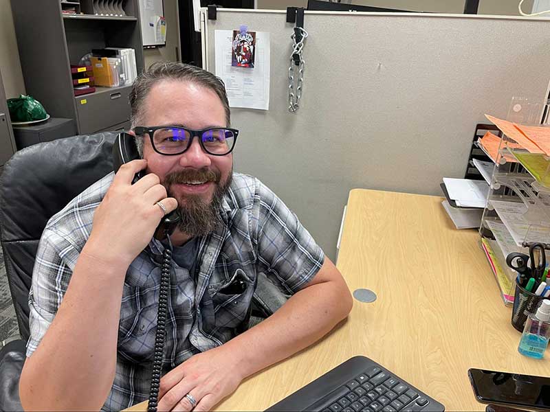 man with beard and glasses  sitting at a desk and talking on the phone