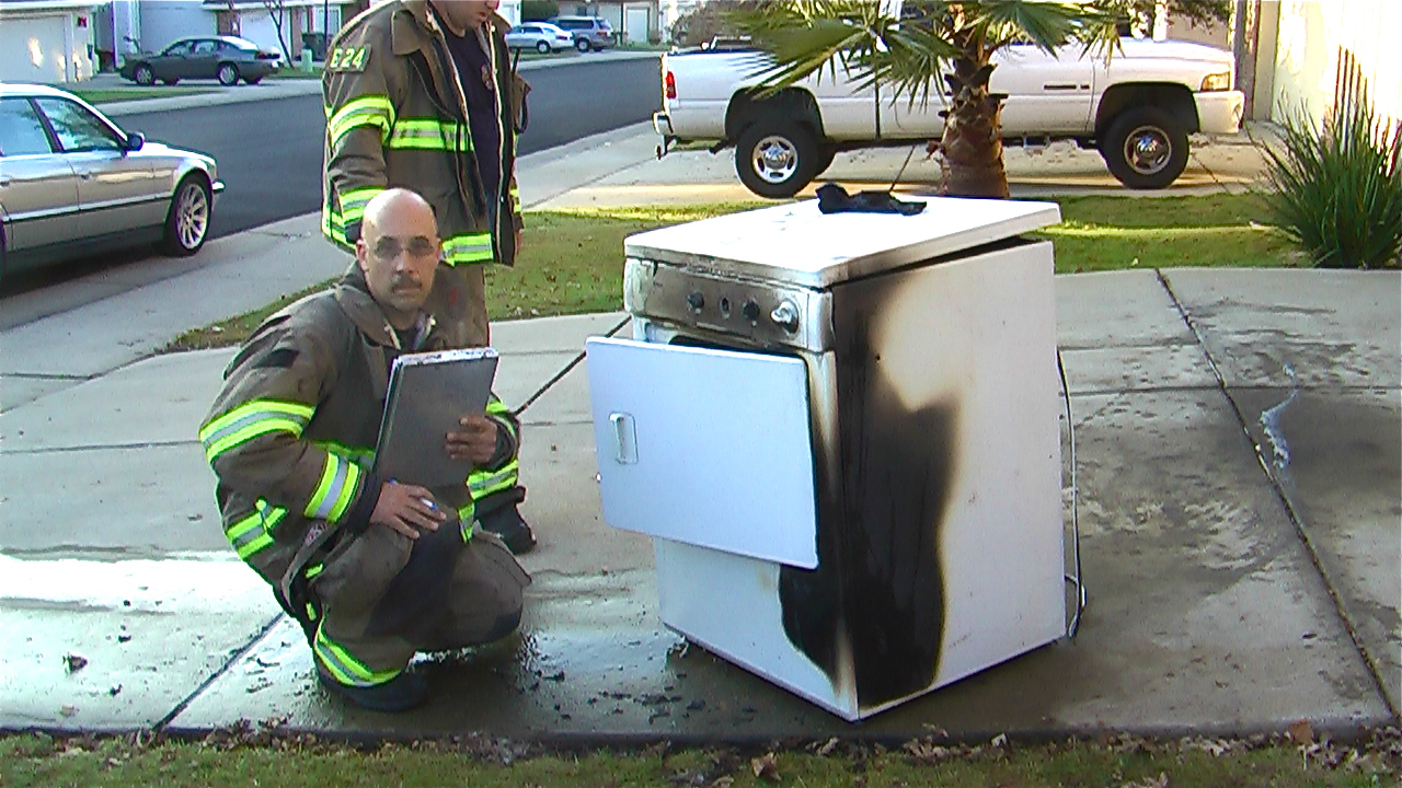 Firefighter kneeling next to dryer with fire damage