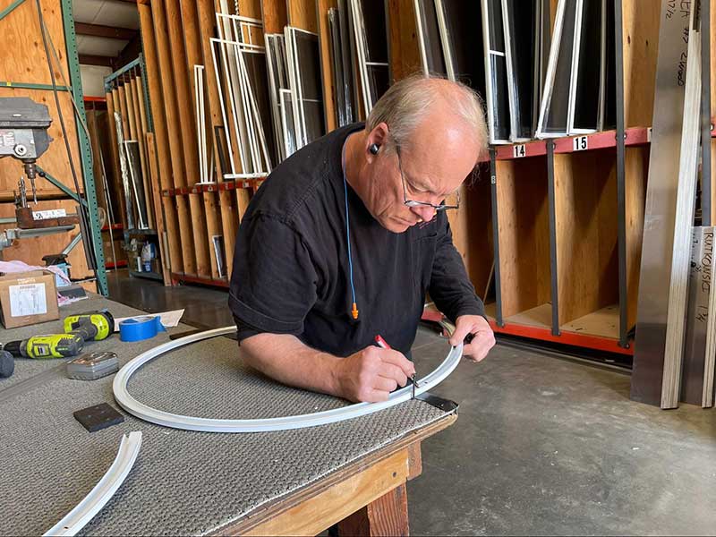 Older man with glasses leaning over a work bench measuring 