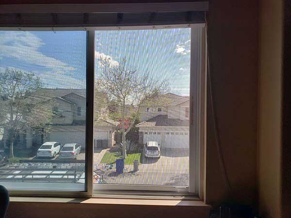 view through two window screen across the street to neighboors home we see cars in their driveways